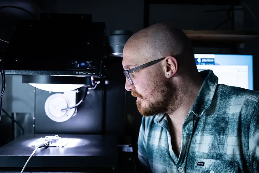 Nate Davis looking at a solar simulator with one of their devices under it Nate Davis looking at a solar simulator with one of their devices under it